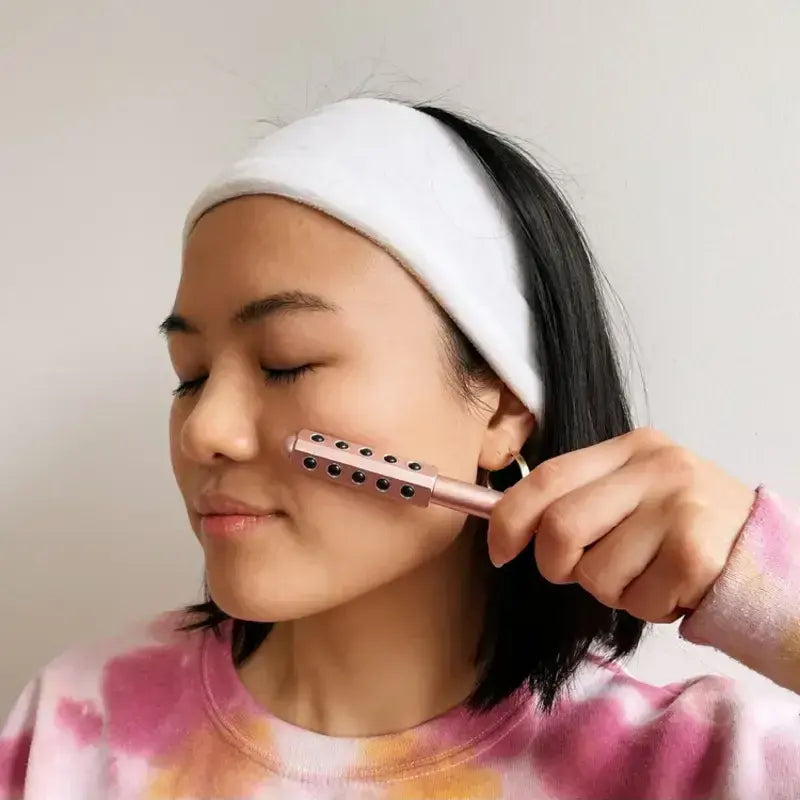 New Magna GermaBelle Roller Pro - Germanium Beauty Face Roller - Woman with spa headband rolling germanium beauty bar along cheekbone during relaxing skincare facial massage routine