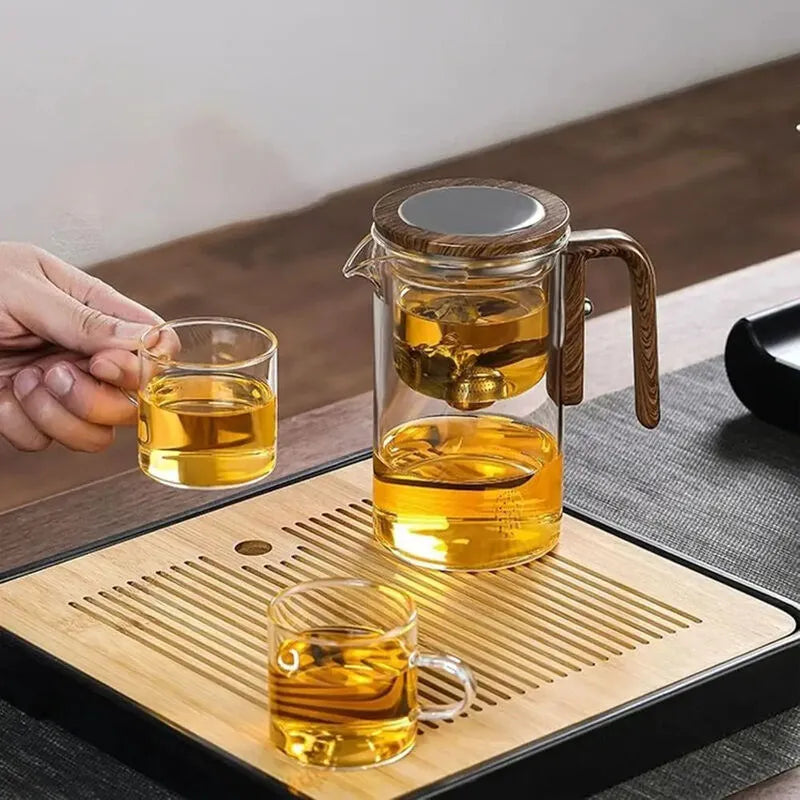 New Magna TeaZen Pro glass teapot with wooden handle on bamboo tea tray with two glass cups filled with golden brewed tea - gravity infusion teapot showing separated tea leaves in upper chamber - elegant tea ceremony setup